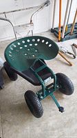 Side view of green metal garden seat frame with four thick rubber tires and a metal turn bar.
