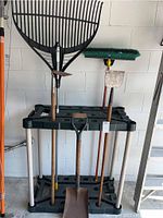 Full view of the four gardening tools arranged on a black and white plastic rack against a white wall.