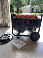 Front and right-side view showing generator, two-wheeled frame, folding handle, power cord and manual on floor