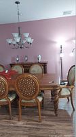 Dining table with eight wooden dining chairs in a room with pink walls and wood floor. Chairs have oval backrests with carved lattice design and cushioned seats.
