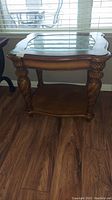 Full front view of the wooden side table showing carved sculpted legs and glass top.