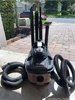 Front view of the RIDGID portable wet/dry vacuum with attachments on the back and hose attached to the front.