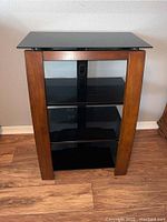 Full view of shelving unit showing wooden legs, black glass shelves, and central metal support.