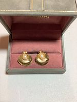 Pair of gold earrings in a box with a pink velvet insert, shaped like shells with a pearl in the middle.