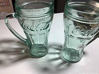 Two green-tinted Coca-Cola glasses side by side showing embossed logo and handles.