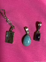 Three small sterling silver pendants with paua shell, larimar, and amethyst stones displayed on pink fabric.