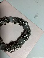 Bracelet composed of several silver toned interlocked loops with grey beads spaced between loops, elastic style.