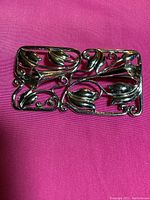Front top view of a rectangular sterling silver floral pin with openwork, shows detailed leaves and flower buds in polished silver against pink background.