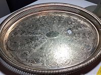 Top side of an oval silver-plated tray showing ornate engraving and beaded rim detail with light tarnishing.