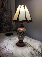 Photo of Japanese themed lamp on fabric surface with clear view of stained glass shade and ceramic base.