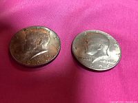 Obverse side of two JFK half dollar coins showing Kennedy's profile and the years 1964 and 1979.