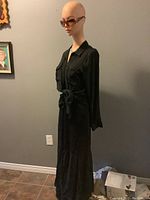 Photo of mannequin wearing black long sundress with sheer ruffle hem and sunglasses, side angled view
