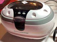Front view of the Magnasonic ultrasonic jewelry cleaner showing on and off buttons, transparent lid, white and gray body.