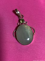 Close-up photo of the sterling silver pendant with large oval green quartz cabochon and small round peridot above it, shown on pink background.