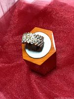 Close-up of gold-toned rhinestone band ring with crisscross rows of clear stones on a wooden display stand against red fabric background.