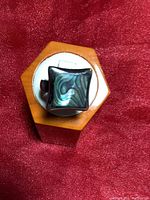 Top view of a square Paua shell inlay ring set in sterling silver on a display stand.