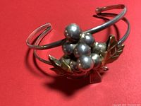 Close-up image of the sterling silver bracelet showing the grape cluster centerpiece with silver berries and gold toned leaves on a red background.