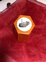 Front view of sterling silver buckle ring displayed on hexagonal wooden display stand with white cushion, placed on red fabric
