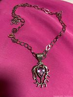 Full view of sterling silver chain with amethyst pendant on pink background.