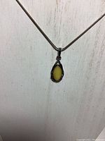 Front view of sterling silver chain with butter amber pendant hanging on a textured white background.