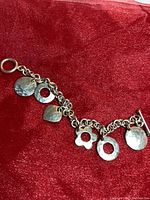 Top view of sterling silver hammered link charm bracelet with charms on red fabric.