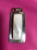 Front view of rectangular sterling silver pendant with mother of pearl inlay and five-ring bale on pink background.