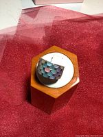 Wide band sterling silver ring with a pastel geometric pattern in hexagonal shapes, on white cushion and wooden display stand.