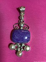 Front view of pendant showing central rectangular polished purple stone and five pearls with detailed silver setting.