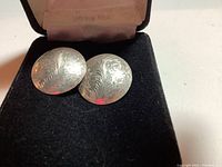 Pair of round sterling silver earrings in a display box showing engraved front surface.