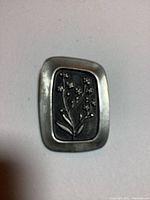 Front view of rectangular pewter brooch with floral design in relief.