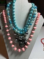 Full view of all three beaded necklaces displayed on a white mannequin stand, showing different bead colors and materials.