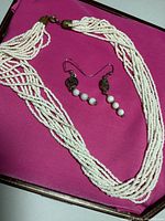 Photo of white multi-strand seed bead necklace and matching earrings on pink surface.