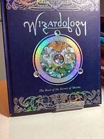 Front cover close-up of 'Wizardology: The Book of the Secrets of Merlin' showing detailed embossed and holographic design.