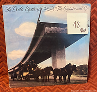 Front cover of The Doobie Brothers vinyl record titled 'The Captain and Me', showing the horse-drawn carriage artwork, with a visible grading sticker VG+ on the coverage