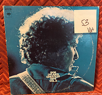 Front of album cover showing Bob Dylan playing harmonica, with a sticker noting grading and condition