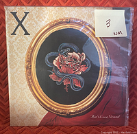 Front of vinyl record cover showing detailed artwork with rose and snake inside a gold oval frame on patterned background.