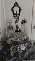Antique cruet set displayed on countertop showing metal stand with four glass containers and various lids, one stopper missing.