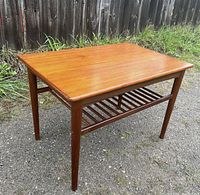 Three-quarter view showing teak tabletop, slatted lower shelf, and tapering legs