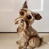 Front view of the dog lamp showing detailed porcelain fur texture, expressive orange-brown glass eyes, and cream to brown glaze.