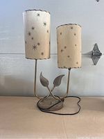 Front view of lamp showing two cylindrical fiberglass shades with starburst patterns and brass base with leaf accents.