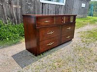 Side angle of the vintage mid-century modern wooden dresser showing wood grain and gold-tone handles.