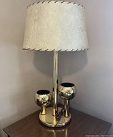 Front view of the lamp showing the two brass planter spots, the central brass column, and the cream-colored fiberglass shade with gold stars and black stitching.