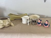 Overview shot of all items in lot including planters, milk glass vase, ceramic bowl, and salt and pepper shakers on beige cloth.