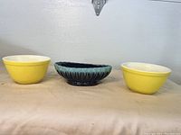 Front view showing two yellow Pyrex bowls flanking a blue-green ribbed ceramic planter.