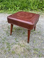 Side view of brown vinyl ottoman showing tapered wooden legs and embossed top.