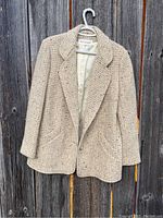Full front view of vintage Holt Renfrew women's knit jacket hanging on a hanger, shown against a wooden fence background.