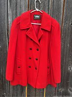 Full front view of bright red vintage peacoat jacket hanging on white hanger against wooden backdrop