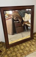 Full view of the vintage mirror standing against a wall showing the entire wooden frame and reflective surface.