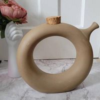 Side view of circular beige pottery wine tote with cork stopper and spout, showing shape and design
