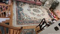 Overview of the carpet laid out in a living area showing its size and multicolor floral pattern with fringe edges.